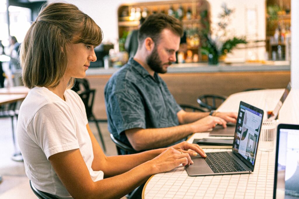 Two young professionals working on laptops in a modern cafe setting.